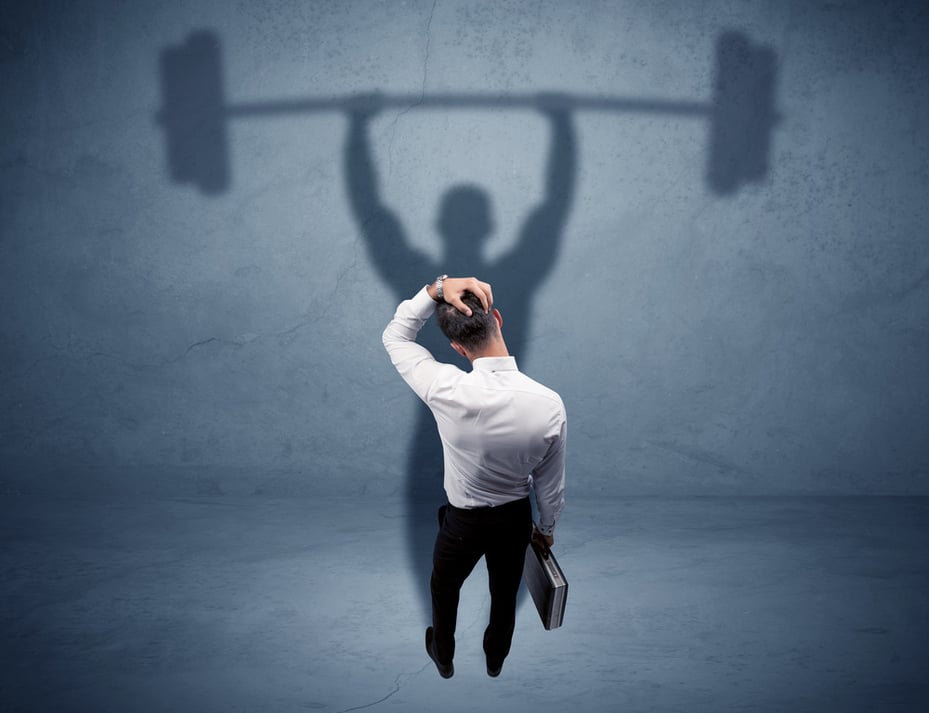 A confident young elegant salesman with briefcase facing a wall, looking at his strong, weight lifting shadow concept